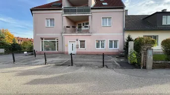 Gebäudeansicht mit rosa Fassade, mehreren Balkonen und einem kleinen Vorgartenbereich.