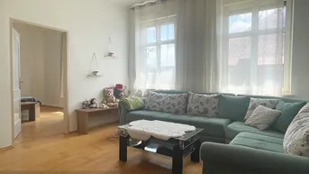 Helles Wohnzimmer mit grünem Ecksofa, Holzboden und großen Fenstern, die viel Tageslicht hereinlassen.