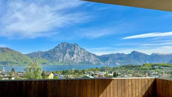 Panoramablick von einem Balkon mit Holzverkleidung auf einen See und majestätische Berge.