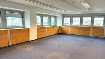 Geräumiges Büro mit Teppichboden, vielen Fenstern und Holzverkleidungen unter den Fensterbänken.