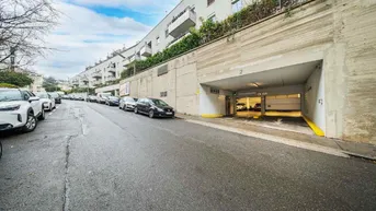 Eingang zur Tiefgarage von der Straße aus, umgeben von einem Wohngebäude und parkenden Autos.