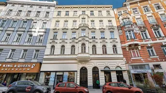 Klassisches Wiener Wohnhaus mit reich verzierter Fassade und Geschäften im Erdgeschoss an einer belebten Straße.