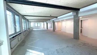 Heller, offener Büroraum mit langen Fensterreihen und Betonboden, der viel Tageslicht hereinlässt.