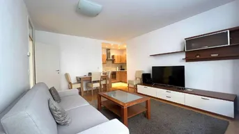 Heller Wohn- und Essbereich mit Sofa, Couchtisch und integrierter Küche im Hintergrund.