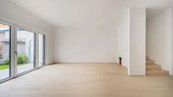 Heller, leerer Wohnbereich mit großen Glasfronten, Zugang zum Garten und offener Treppe.