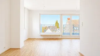 Helles, leeres Zimmer mit Parkettboden und großem Fenster, das auf einen Balkon oder eine Terrasse führt.