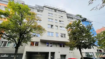 Modernes Mehrfamilienhaus mit vielen Fenstern, Tiefgarageneinfahrt und einer Dachterrasse, umgeben von Bäumen.