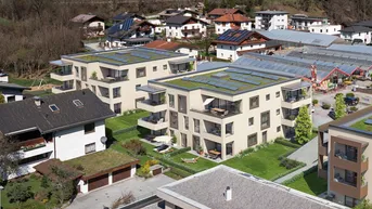 Luftaufnahme einer modernen Wohnanlage mit begrünten Dächern und Solaranlagen in ländlicher Umgebung.
