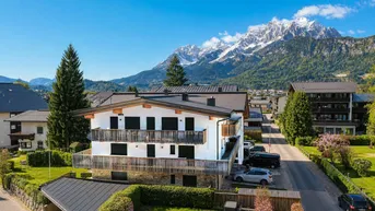 Modernes Mehrfamilienhaus mit Balkonen und beeindruckendem Bergblick in einer grünen alpinen Umgebung.