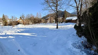 Weitläufiges, schneebedecktes Grundstück mit Blick auf umliegende Häuser und Berge unter blauem Himmel.