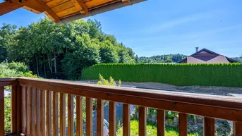 Blick vom Holzbalkon ins Grüne mit weitreichender Aussicht und blauem Himmel.
