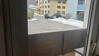 Blick vom Balkon auf die verschneite Straße und umliegende Gebäude mit Bergpanorama im Hintergrund.