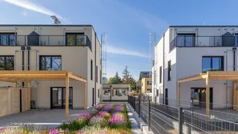 Moderne Reihenhäuser mit Balkonen, Terrassen und gepflegten Außenanlagen unter blauem Himmel.
