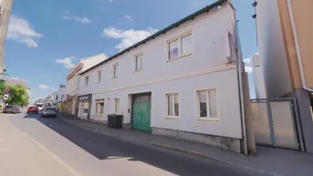 Gebäude mit heller Fassade und grünem Tor an einer städtischen Straße unter blauem Himmel.