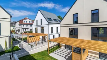 Mehrere moderne Neubauhäuser mit hellen Fassaden und Holzpergolen im Außenbereich.