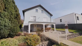 Helles Einfamilienhaus mit überdachter Terrasse, Garten und Grillplatz, umgeben von viel Grün.