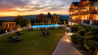 Abendliche Ansicht eines Hotels mit beleuchtetem Pool, Liegewiese und malerischer Landschaft im Hintergrund.