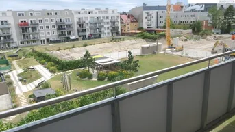 Blick vom Balkon auf eine Grünfläche, weitere Gebäude und eine Baustelle in der Ferne.