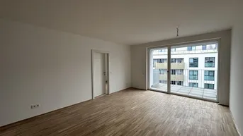 Helles, unmöbliertes Wohnzimmer mit Holzboden und Zugang zu einem Balkon.