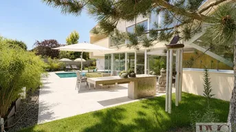 Großzügige Terrasse mit Essbereich, Sonnenschirm und Pool, umgeben von Grünflächen und Bäumen.