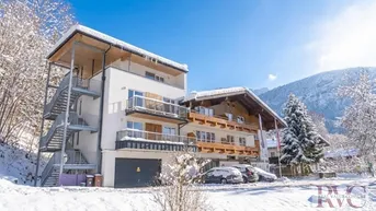 Modernes Gebäude mit Balkonen und Außentreppe, umgeben von verschneiter Winterlandschaft und Bergen.