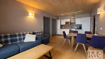 Gemütlicher Wohn-Essbereich mit offener Küche, Holzdecken und modernem Interieur.