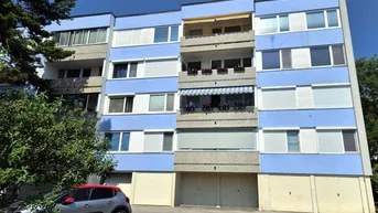 Mehrfamilienhaus mit blauer Fassade, Balkonen und Garagen im Erdgeschoss.