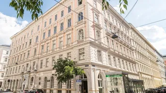 Historisches Eckgebäude mit klassischer Architektur und vielen Fenstern an einer belebten Straße.