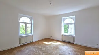 Helles Zimmer mit Fischgrätparkett und zwei großen Rundbogenfenstern, ideal als Wohn- oder Schlafzimmer.