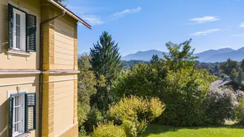 Seitenansicht des Gebäudes mit Blick auf die umliegende grüne Landschaft und ferne Berge.