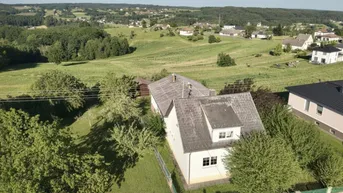 Luftaufnahme eines Hauses mit Satteldach, umgeben von grünen Feldern und ländlicher Bebauung.