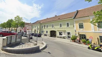 Blick auf eine belebte Straße mit traditionellen Gebäuden und geparkten Autos unter blauem Himmel.