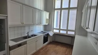 Helle Küche mit weißen Einbauschränken, Holzfußboden und großem Fenster.