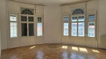 Helles, geräumiges Zimmer mit Fischgrätparkett und hohen Bogenfenstern, ideal als Wohnbereich.