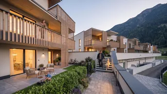 Moderne Wohnanlage mit Terrassen, Balkonen und Blick auf die umliegende Berglandschaft bei Sonnenuntergang.