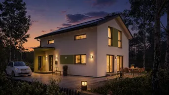 Modernes Einfamilienhaus bei Sonnenuntergang mit beleuchteter Terrasse und Vorgarten.