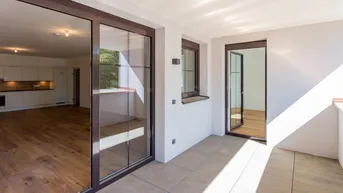 Heller Wohnbereich mit Holzboden und Zugang zur Loggia, die viel Tageslicht hereinlässt.