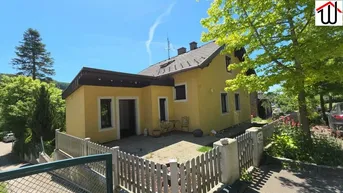 Gelbes Einfamilienhaus mit Satteldach und kleinem gepflasterten Bereich im Vorgarten.