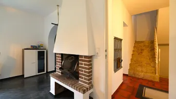 Wohnbereich mit einem gemauerten Kamin und Zugang zu einer Treppe mit Terrakotta-Fliesen.