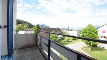 Balkon mit Bergblick und weitem Ausblick über die Dächer der Umgebung unter blauem Himmel.