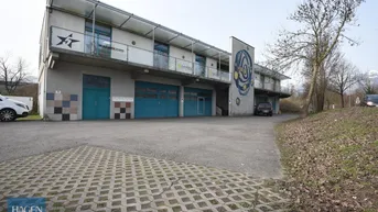 Ansicht des modernen Geschäftsgebäudes mit mehreren Garagentoren und einem großen Parkplatz davor.