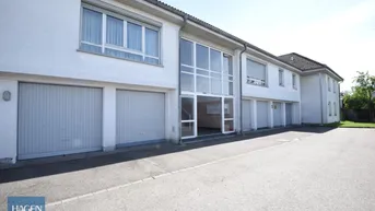Weißes Mehrfamilienhaus mit mehreren Garagen und großen Fenstern im Eingangsbereich.