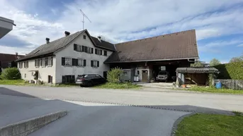 Traditionelles Bauernhaus mit angebautem Scheunenteil und Stellplätzen, umgeben von ländlicher Umgebung.
