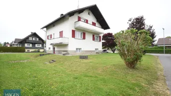 Freistehendes Einfamilienhaus mit weißer Fassade, roten Fensterläden und großem Vorgarten.