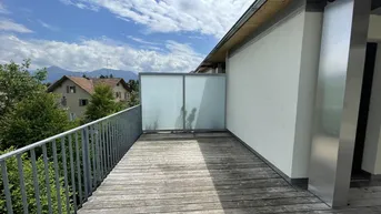 Geräumiger Holzbalkon mit Metallgeländer und weitem Blick auf die umliegende Landschaft und Berge.