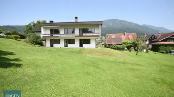 Großzügiges Einfamilienhaus mit weitläufigem Garten und Bergblick unter blauem Himmel.