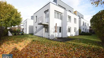 Moderne Wohnanlage mit weißer Fassade und herbstlichem Gartenbereich mit Laub.