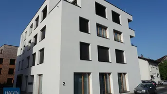 Modernes weißes Mehrfamilienhaus mit klaren Linien und dunklen Fensterläden unter blauem Himmel.