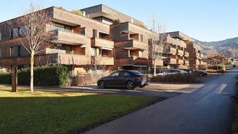 Modernes Mehrfamilienhaus mit Holzschindelfassade, Balkonen und Blick auf die Berge.