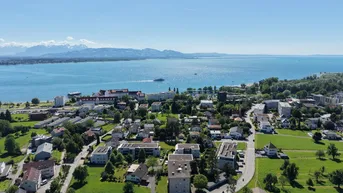 Panoramablick aus der Vogelperspektive auf eine Stadt am See mit Bergen im Hintergrund und grünen Wiesen.